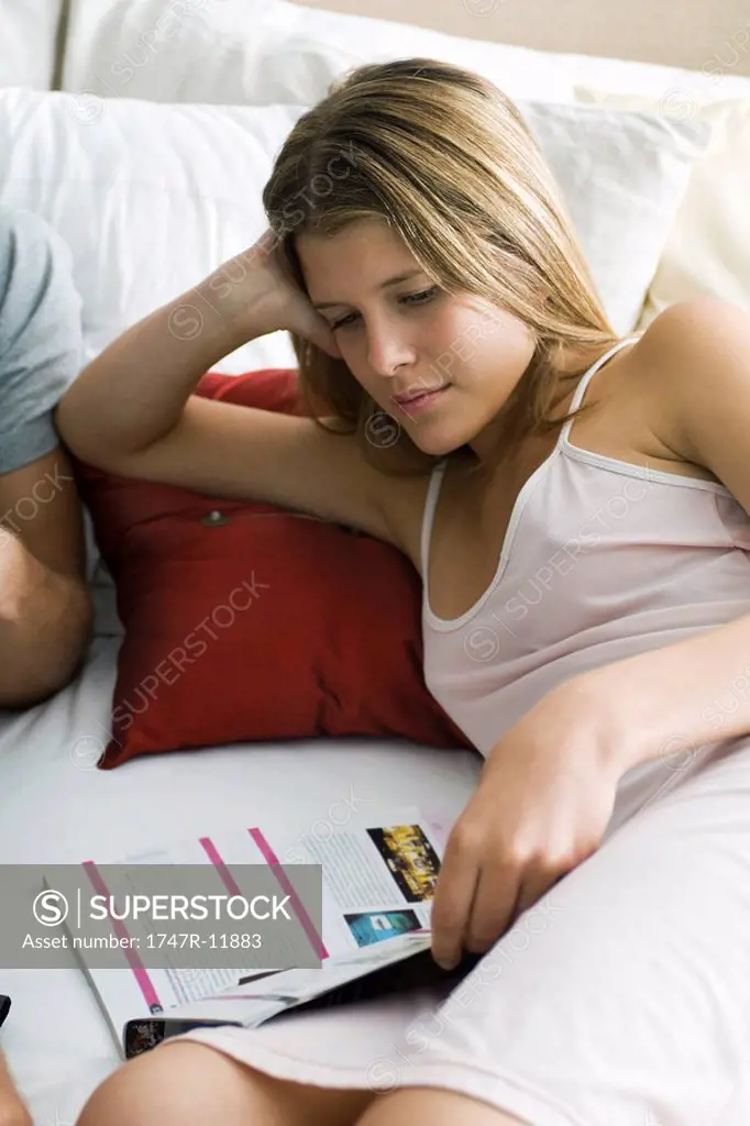 Young woman reading magazine in bed
