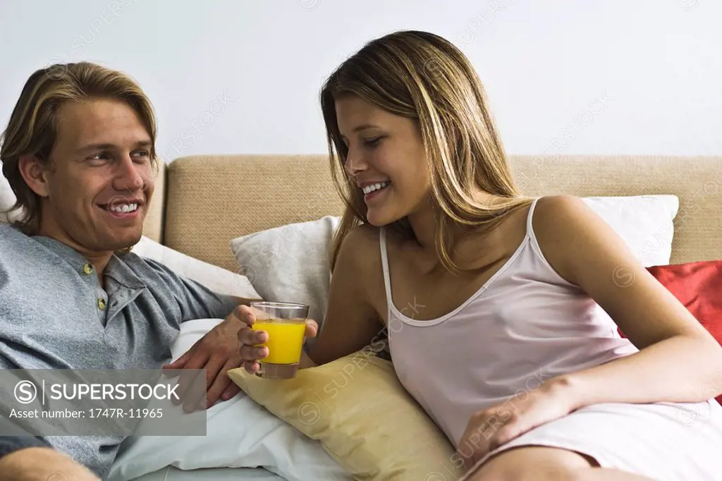 Couple reclining together in bed, woman holding glass of juice
