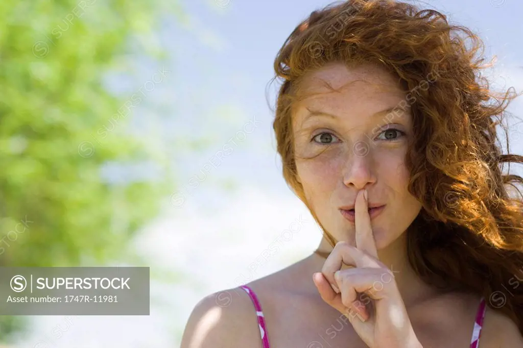 Young woman with finger on lips, portrait