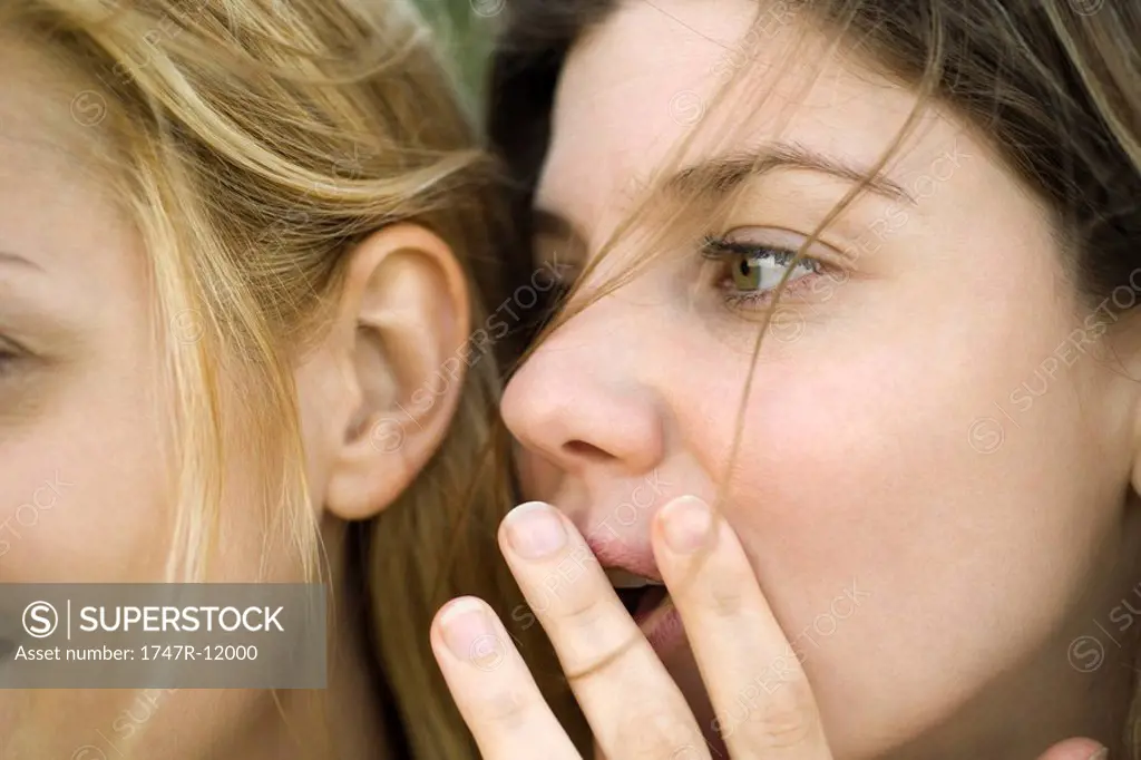 Young woman whispering secret into friend´s ear, close_up