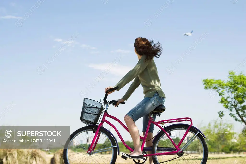 Woman riding bicycle, looking at plane flying in sky