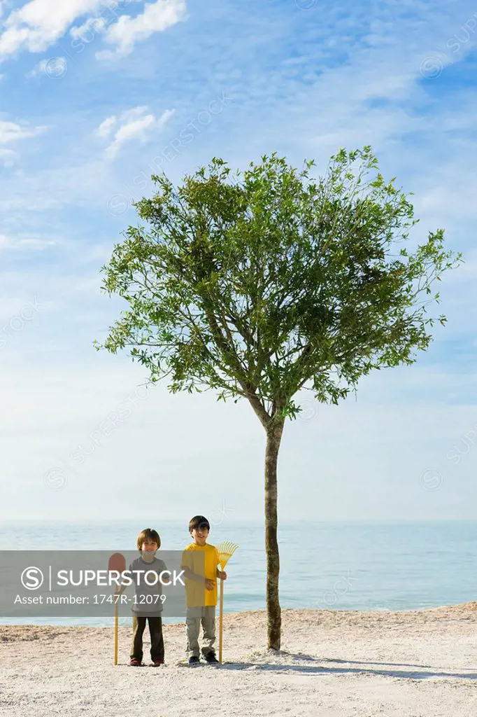 Ecology concept, boys with gardening tools standing by tree growing on beach