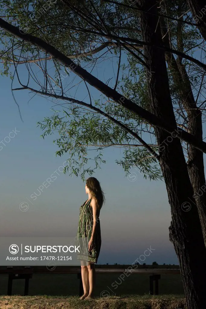 Woman standing outdoors at twilight, looking over shoulder at view