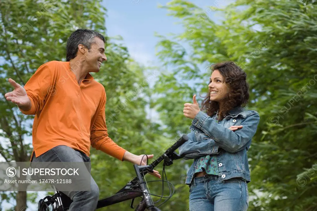 Couple having fun together outdoors, man on bicycle, woman giving thumbs up gesture