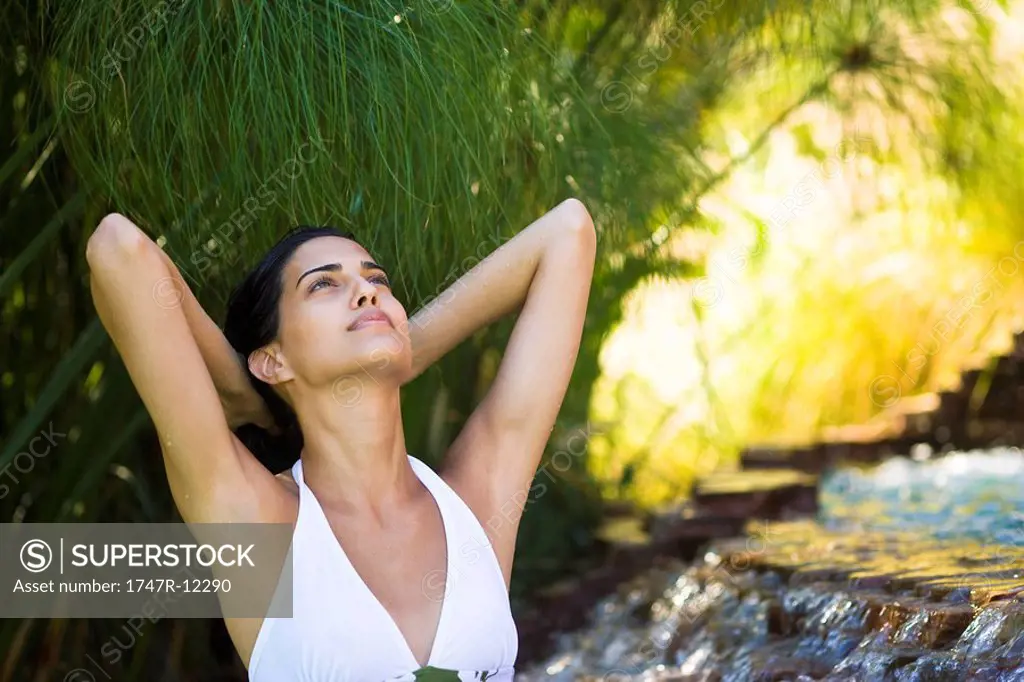 Woman relaxing by waterfall with hands behind head