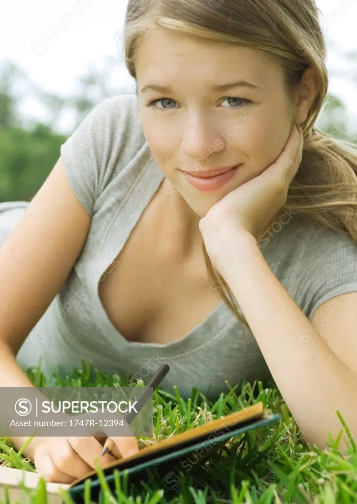 Young woman reclining in grass with notebook and pencil, portrait