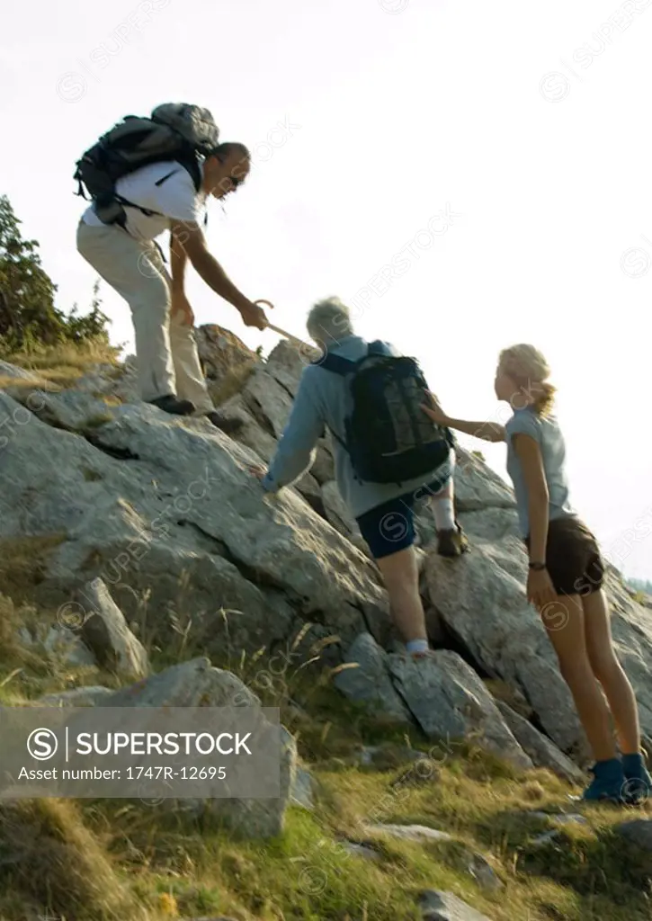 Hikers going up rocks, man and girl helping mature woman