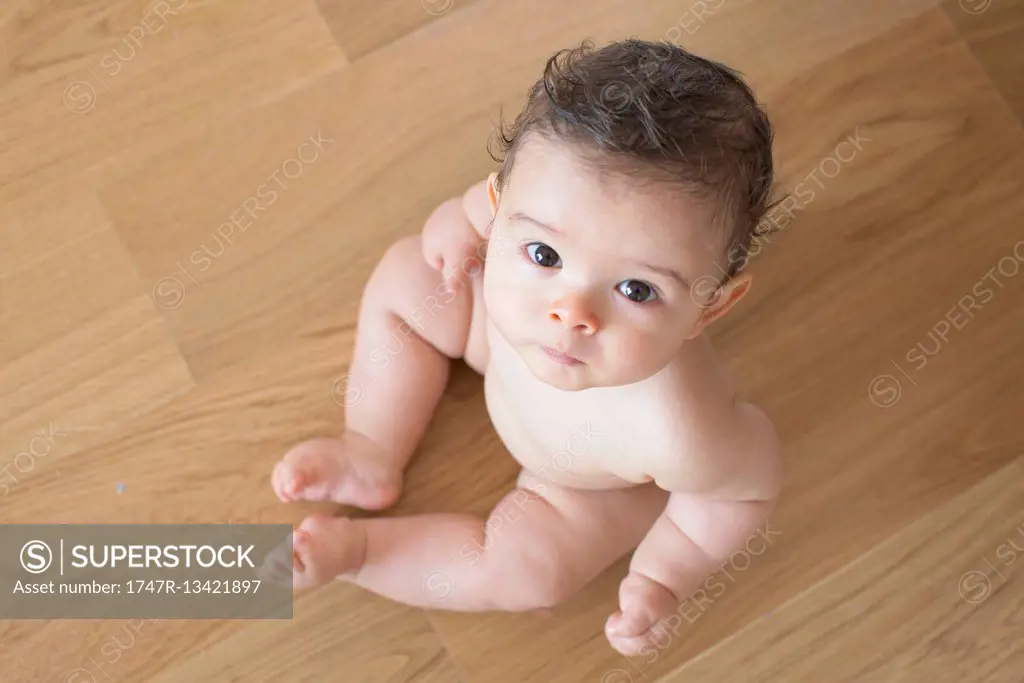 Infant sitting on floor, looking up at camera
