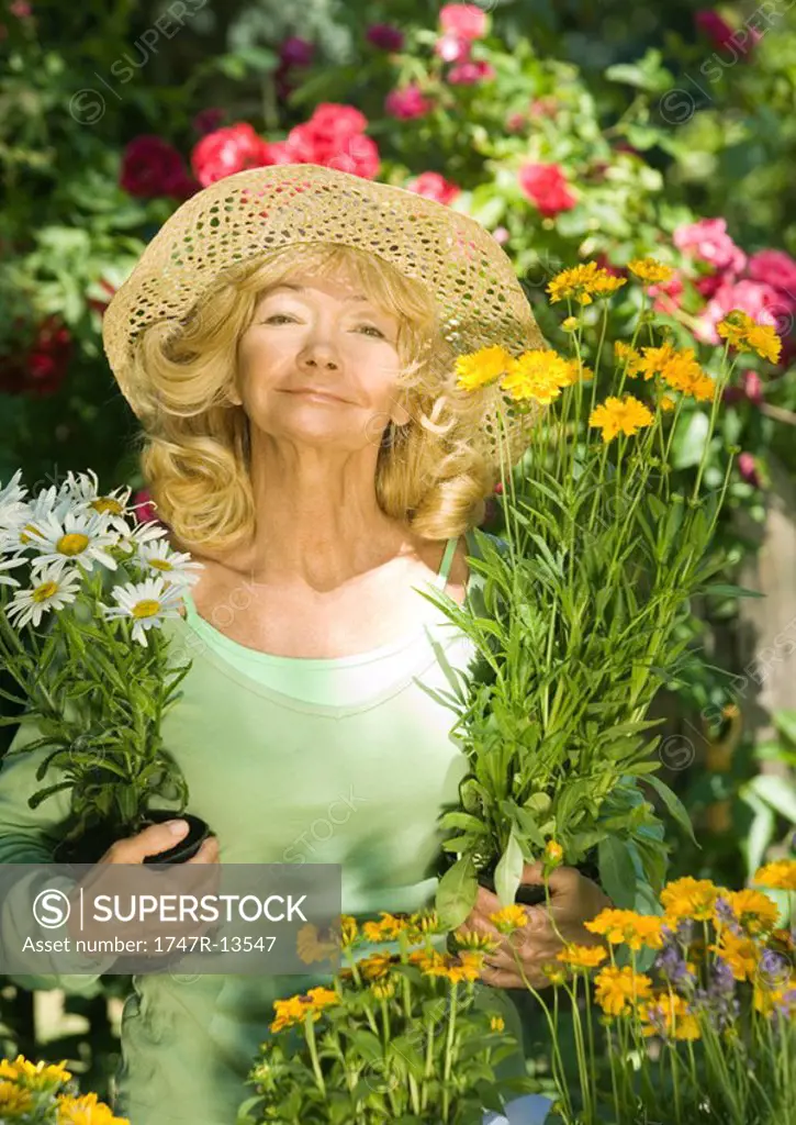 Senior woman holding unpotted flowers, looking at camera