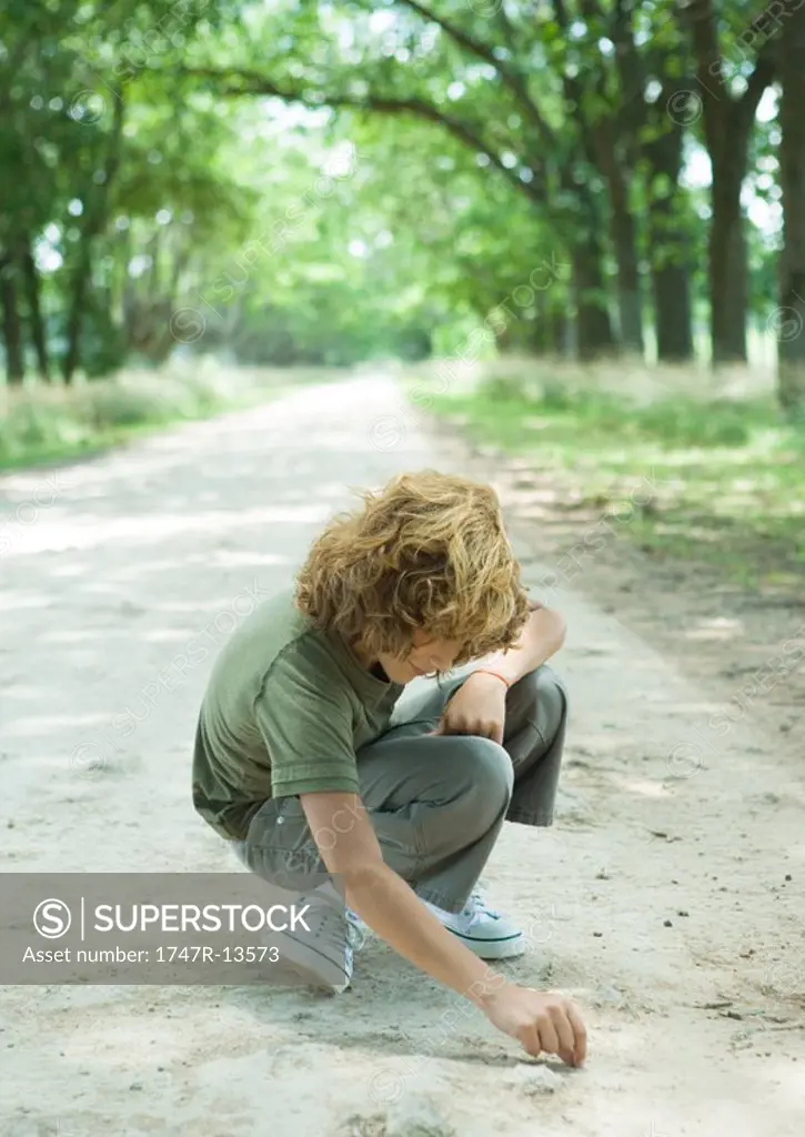 Boy crouching in middle of dirt road