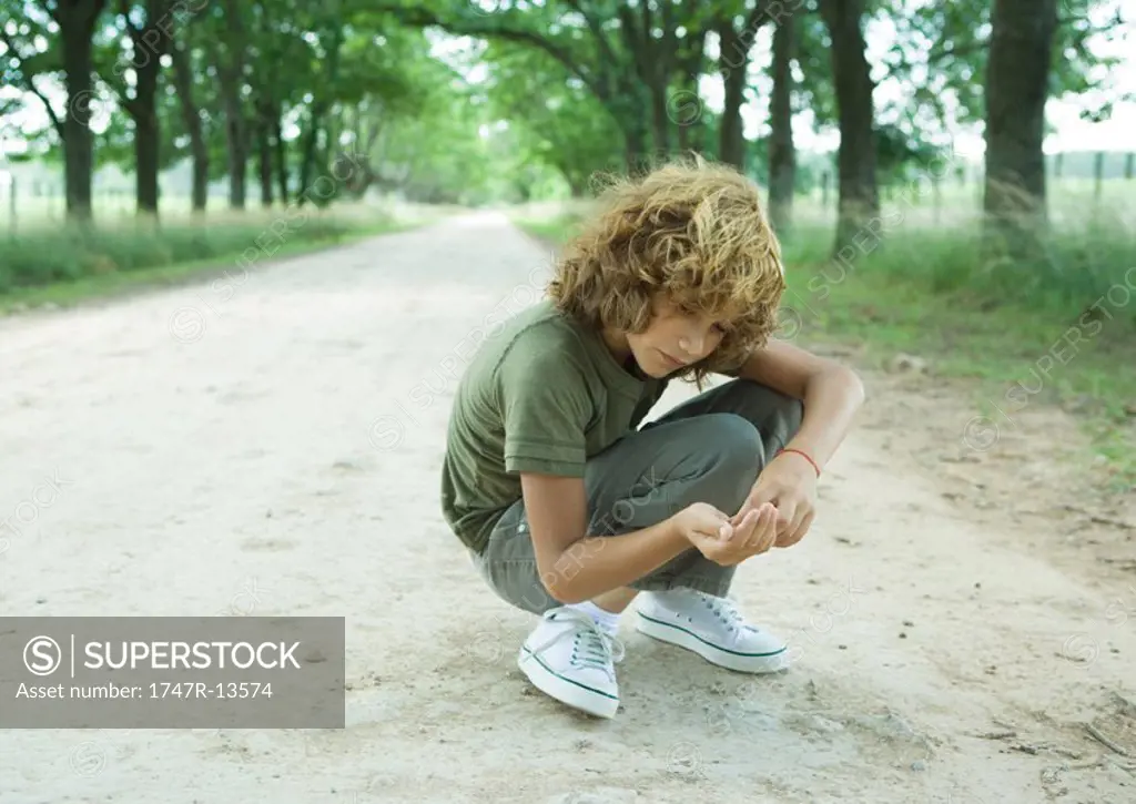 Boy crouching in middle of dirt road, looking at pebbles