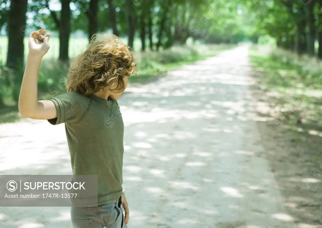 Boy standing in middle of dirt road, throwing pebbles