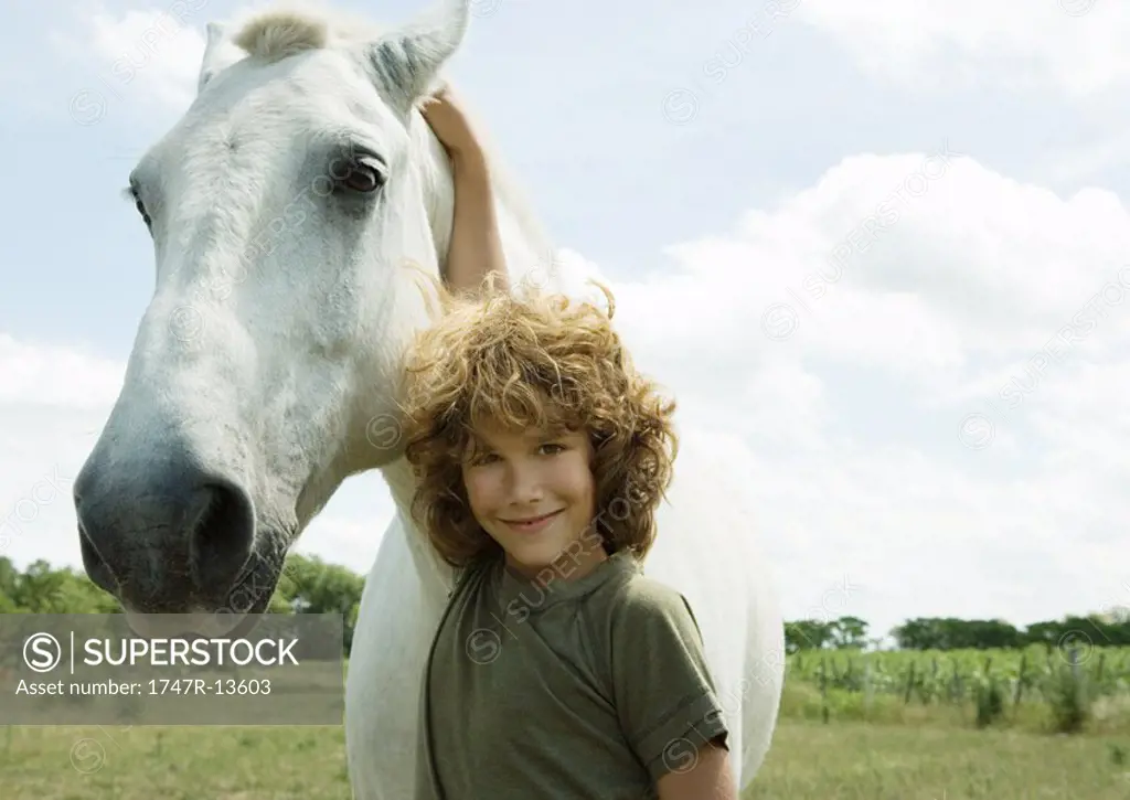 Boy standing with arm around horse