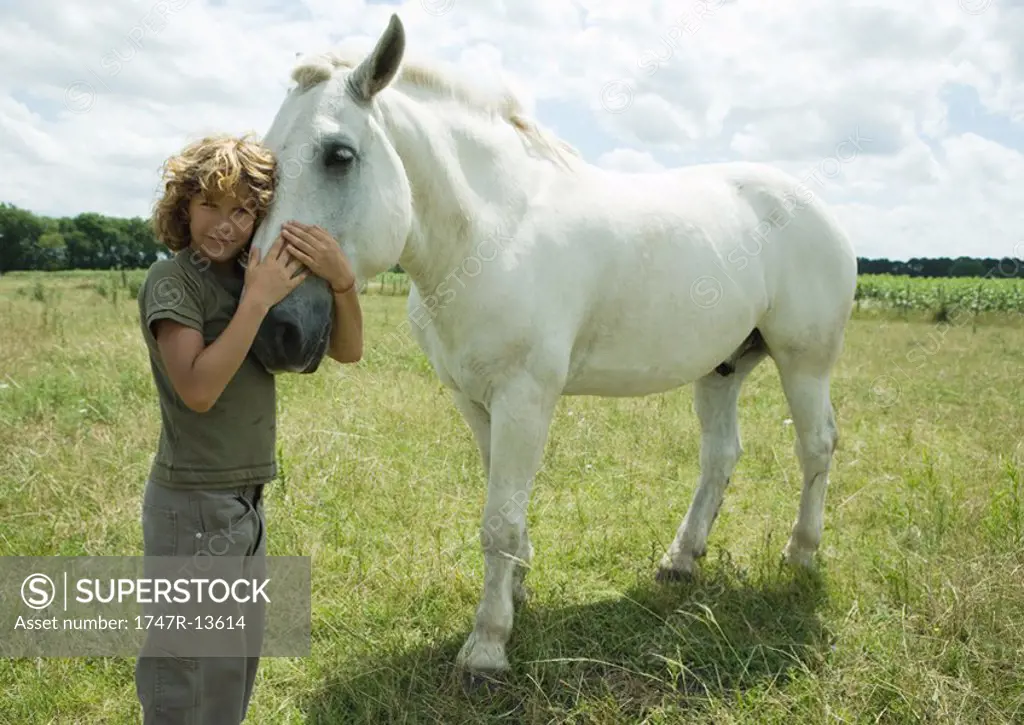 Boy standing cheek to cheek with horse