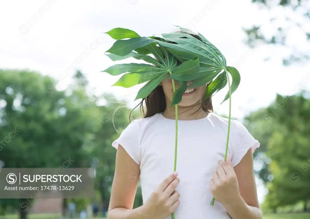 Girl standing holding cassava leaves in front of face