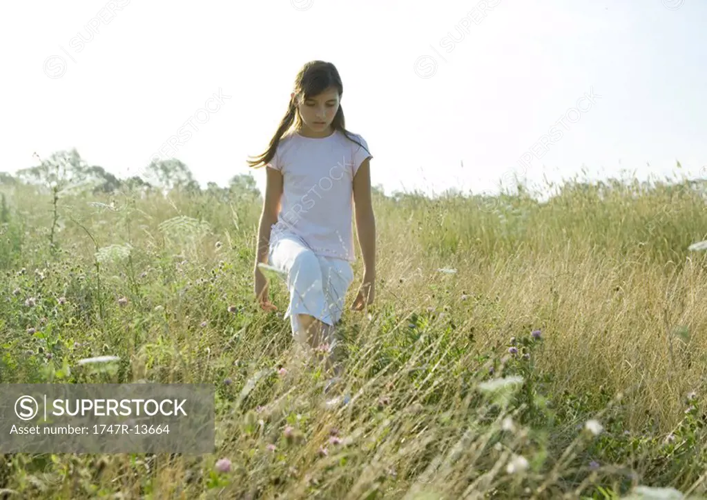 Girl walking through tall grass in field