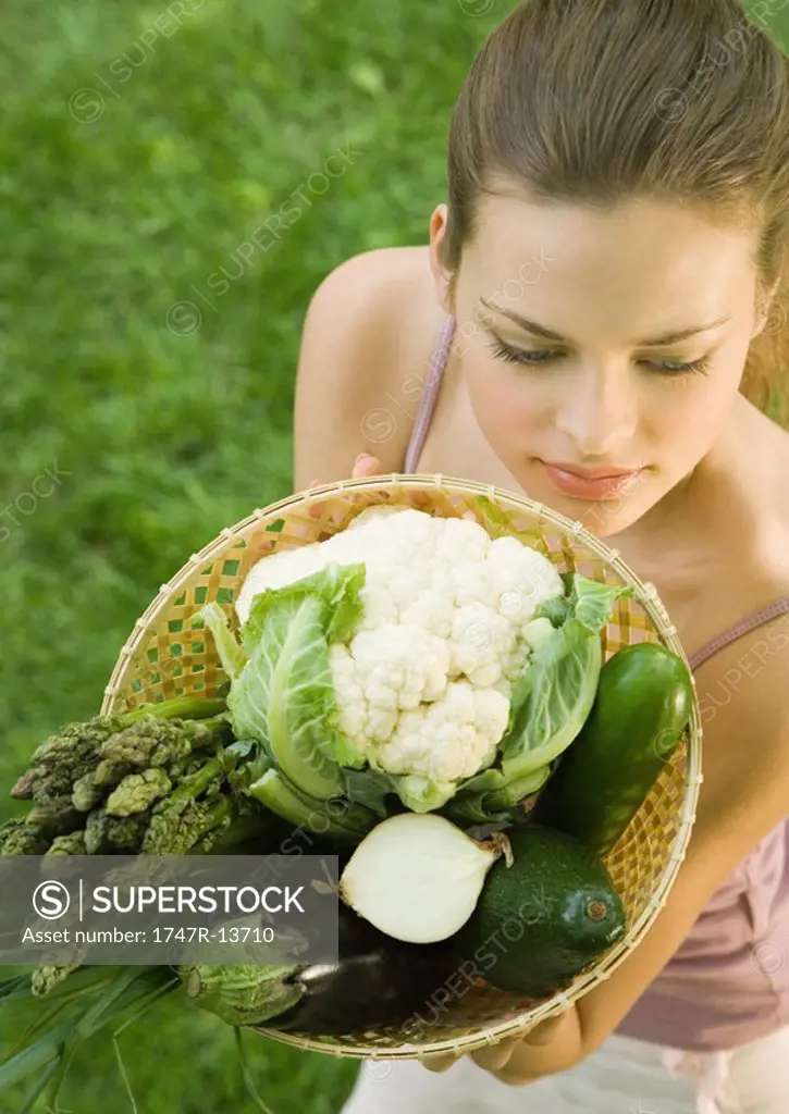 Young woman holding up basket full of vegetables