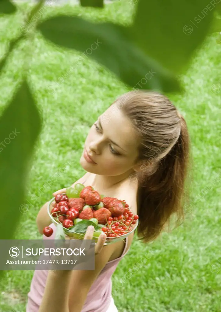 Young woman holding up bowl of fruit