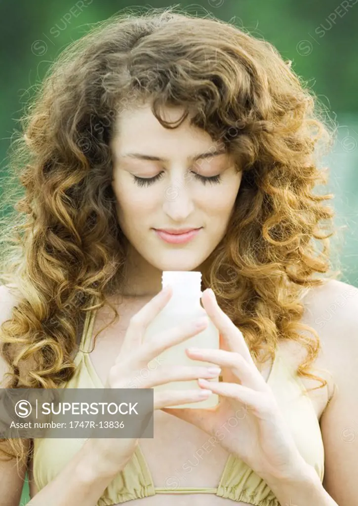 Woman holding up bottle, eyes closed