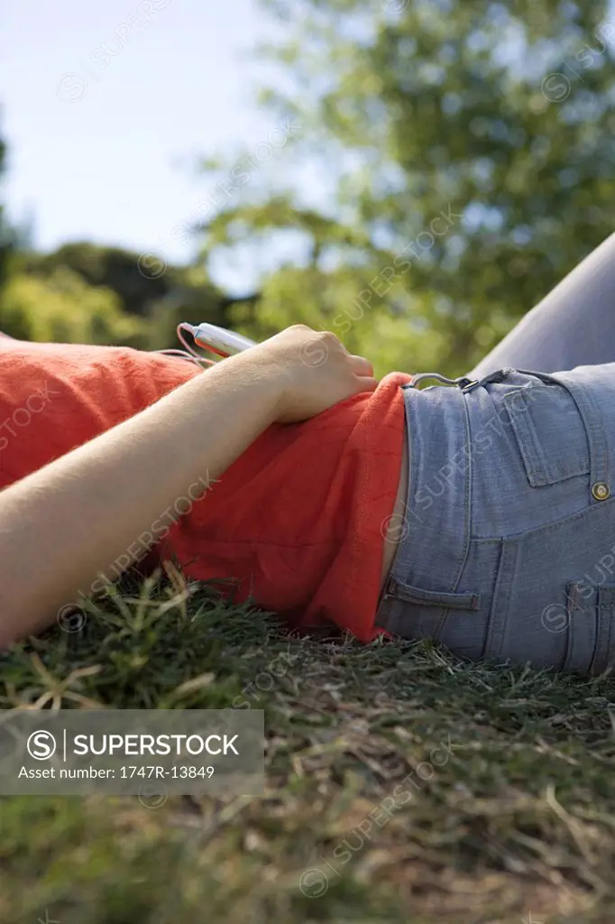 Young woman lying on ground listening to MP3 player, mid section