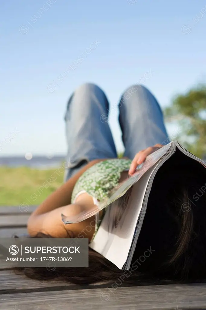 Woman lying on dock with magazine covering her face