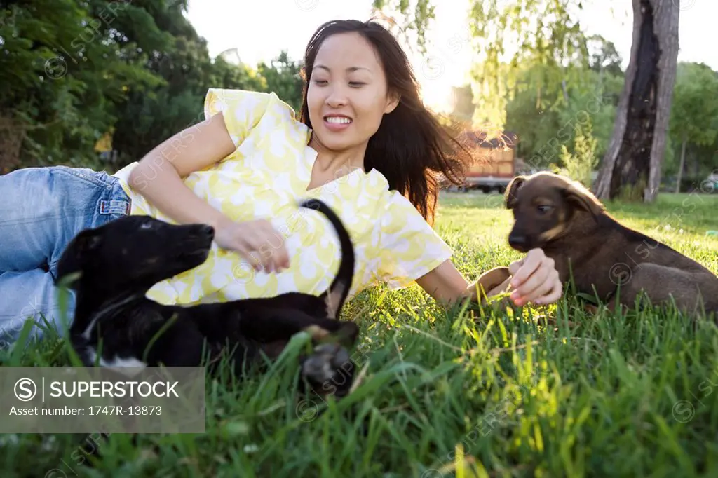 Woman lying in grass playing with two puppies