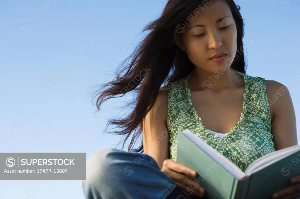 Woman reading book outdoors, hair blowing in breeze