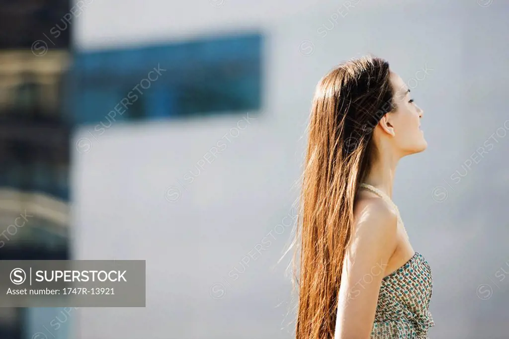 Woman with long hair standing outdoors, eyes closed, side view