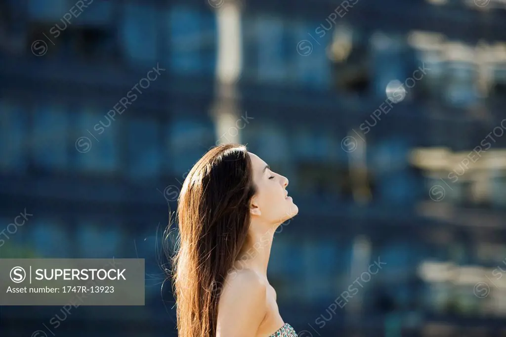 Young woman outdoors on sunny day, head back, eyes closed