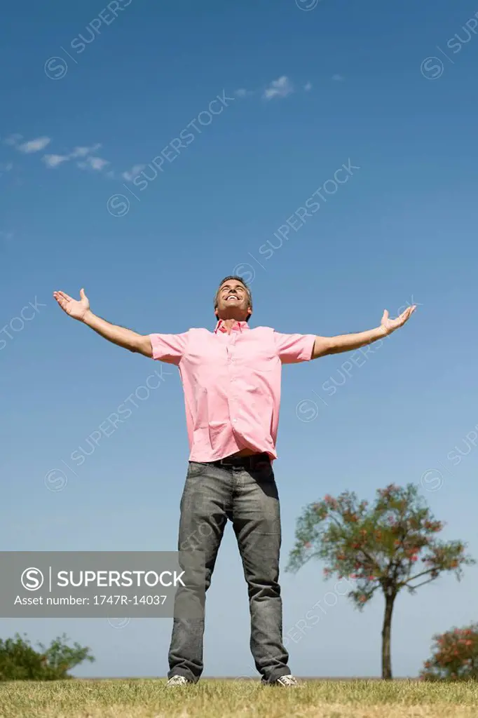 Happy man standing outdoors with arms raised, full length