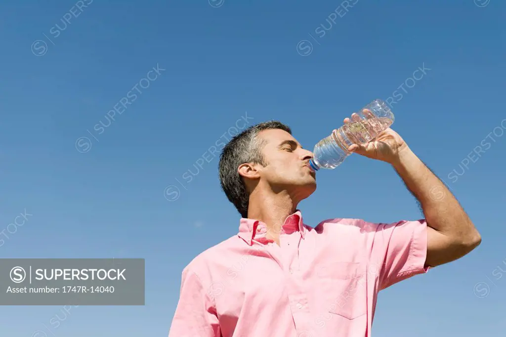 Man standing outdoors drinking from bottle of water, low angle view, blue sky in background