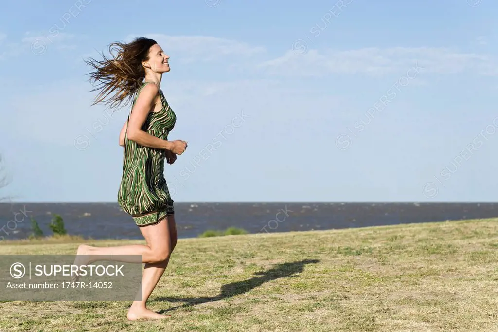 Woman in dress running across grass, barefoot