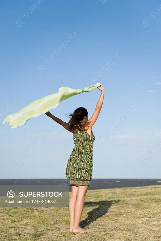 Woman standing outdoors, holding up shawl in wind, full length