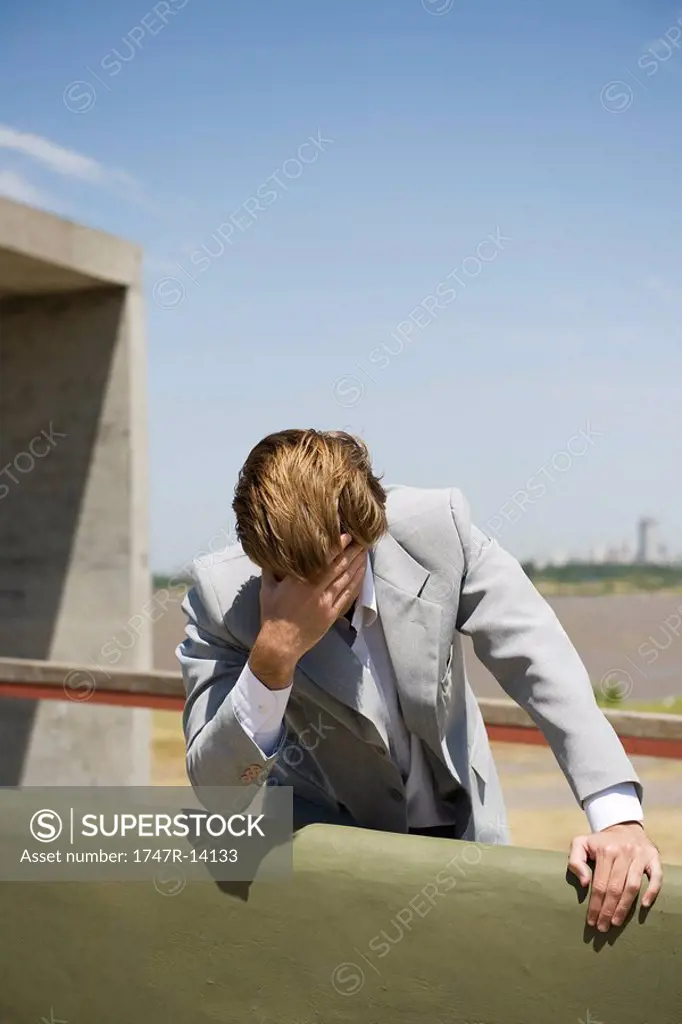Businessman leaning against wall holding head