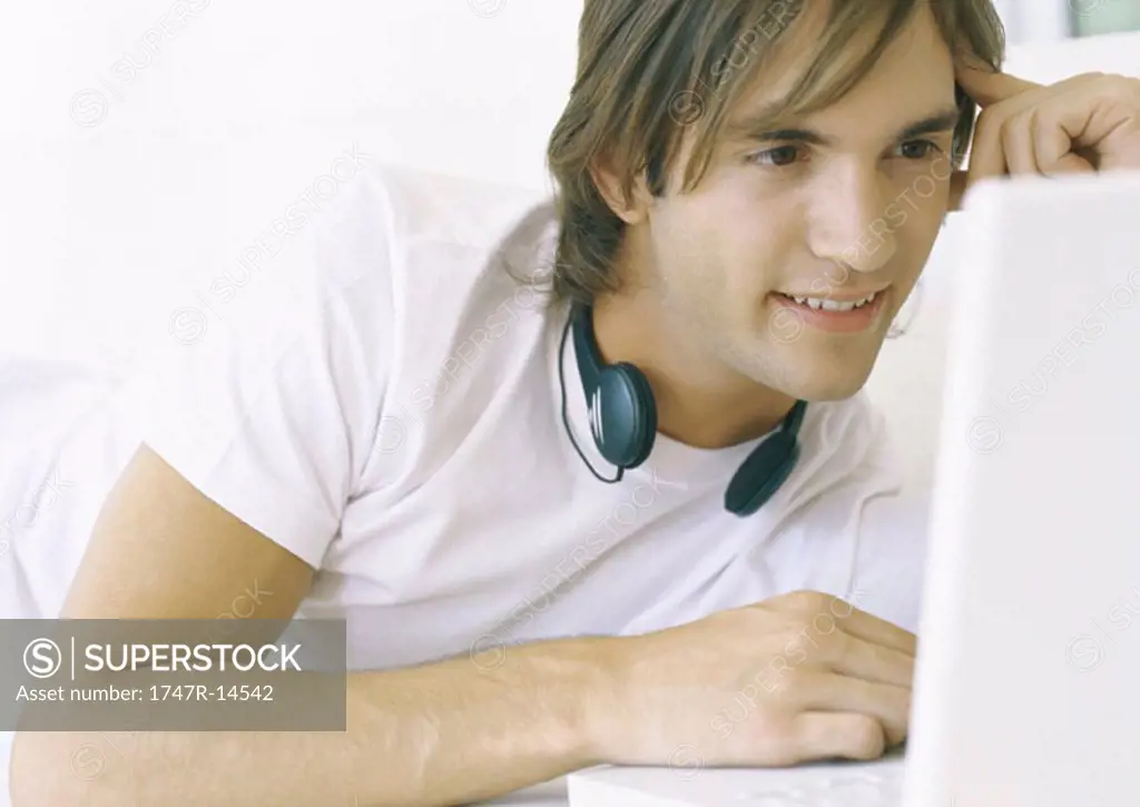 Man using laptop, headphones around neck