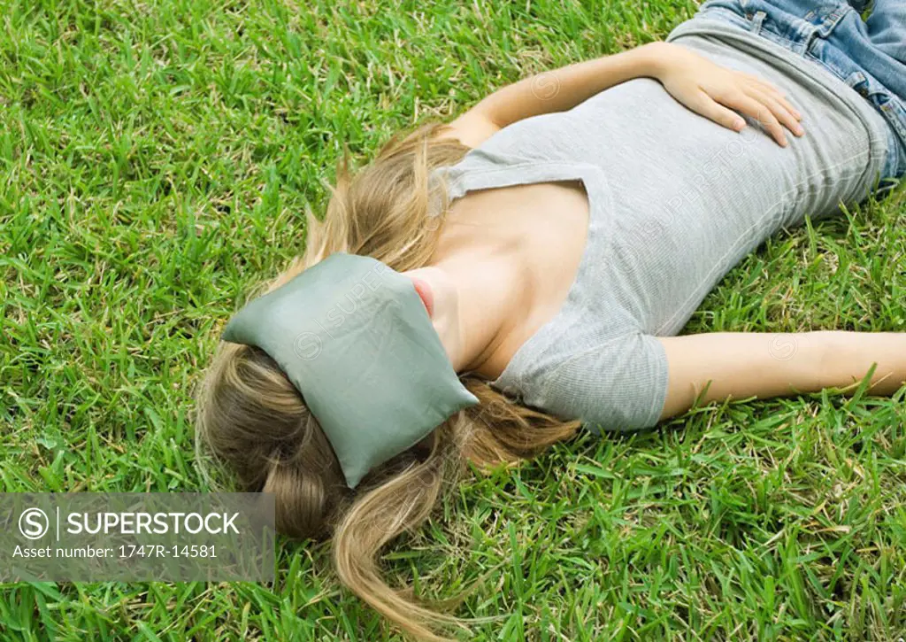 Woman lying in grass with eye pillow over eyes