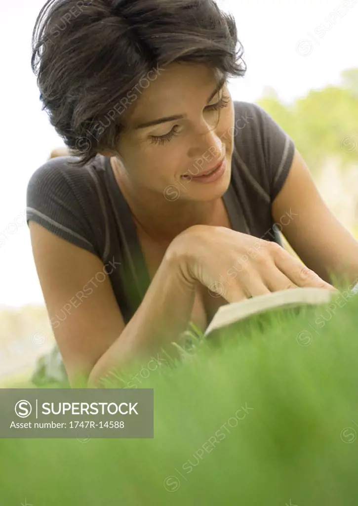 Woman lying in grass, reading