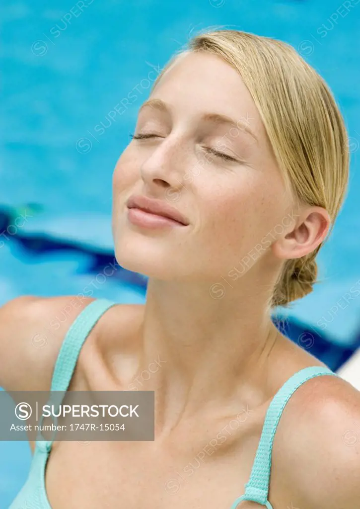 Young woman smiling with eyes closed and head back, portrait, pool in background