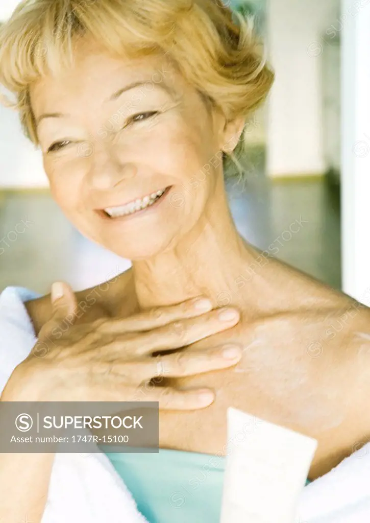 Senior woman applying moisturizer to chest