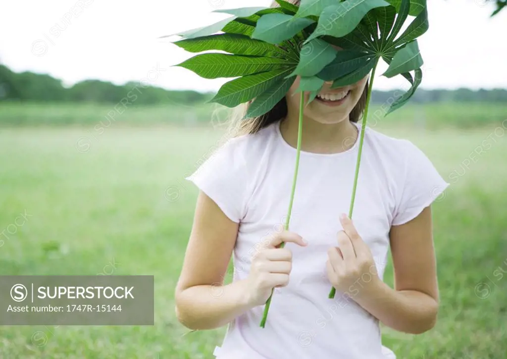 Girl holding up cassava leaves in front of face