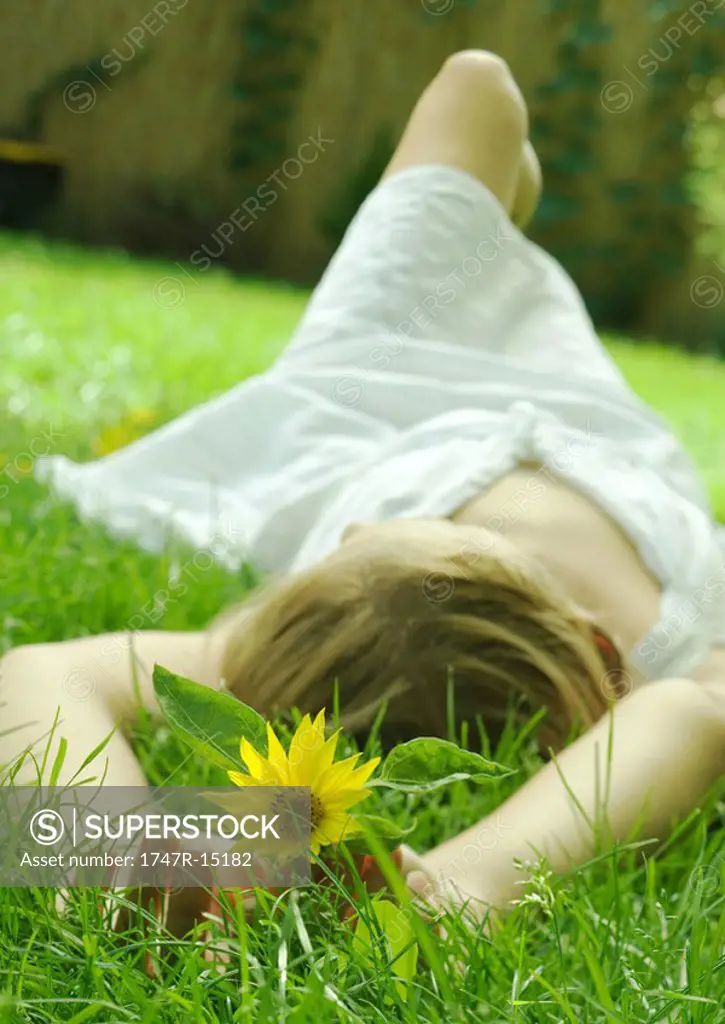 Woman lying in grass, holding flower