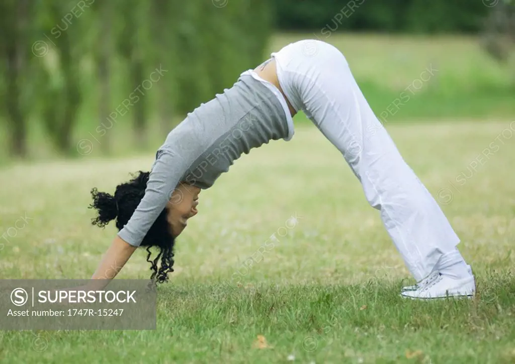 Young woman doing downward dog pose on grass