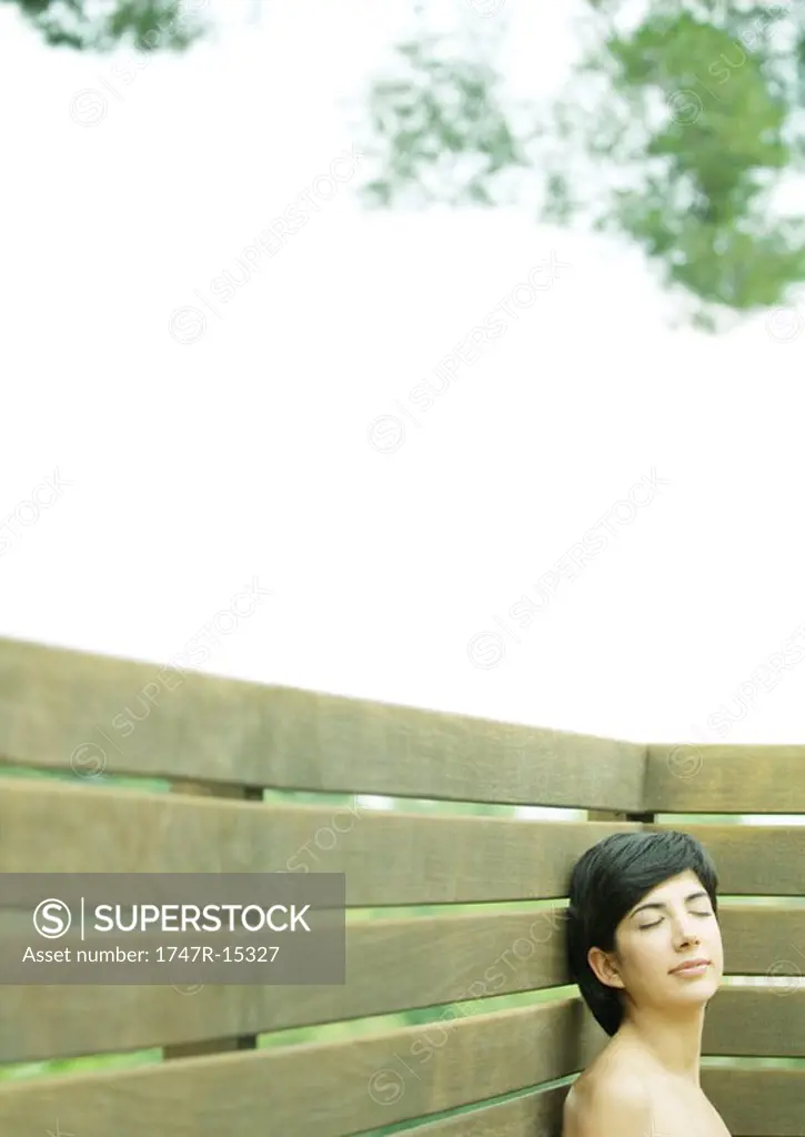 Woman leaning head against wooden enclosure, eyes closed