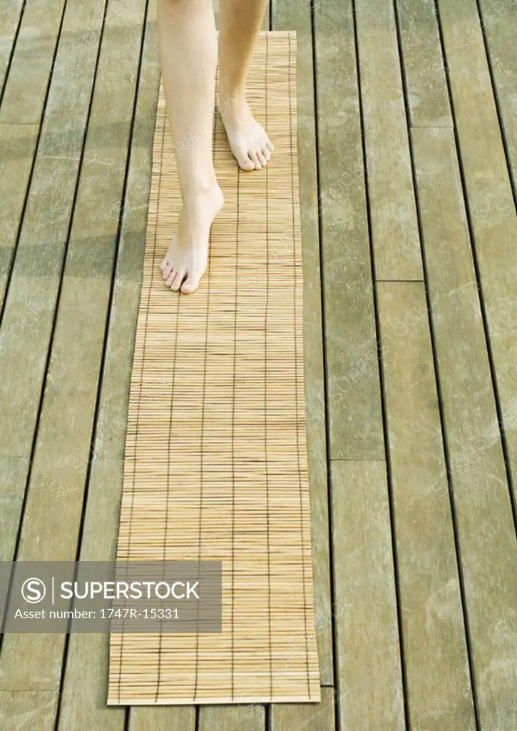 Woman walking on bamboo mat, knee down