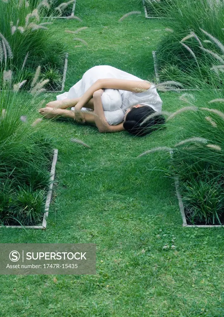 Woman lying on grass, curled up, in ornamental garden