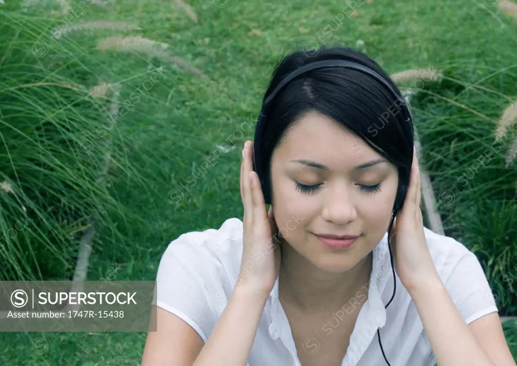 Woman sitting in ornamental garden, listening to headphones