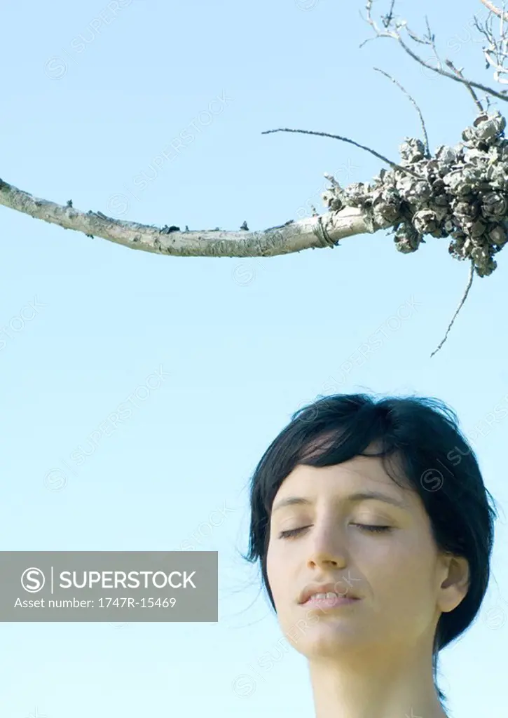 Woman standing under dry branch, eyes closed