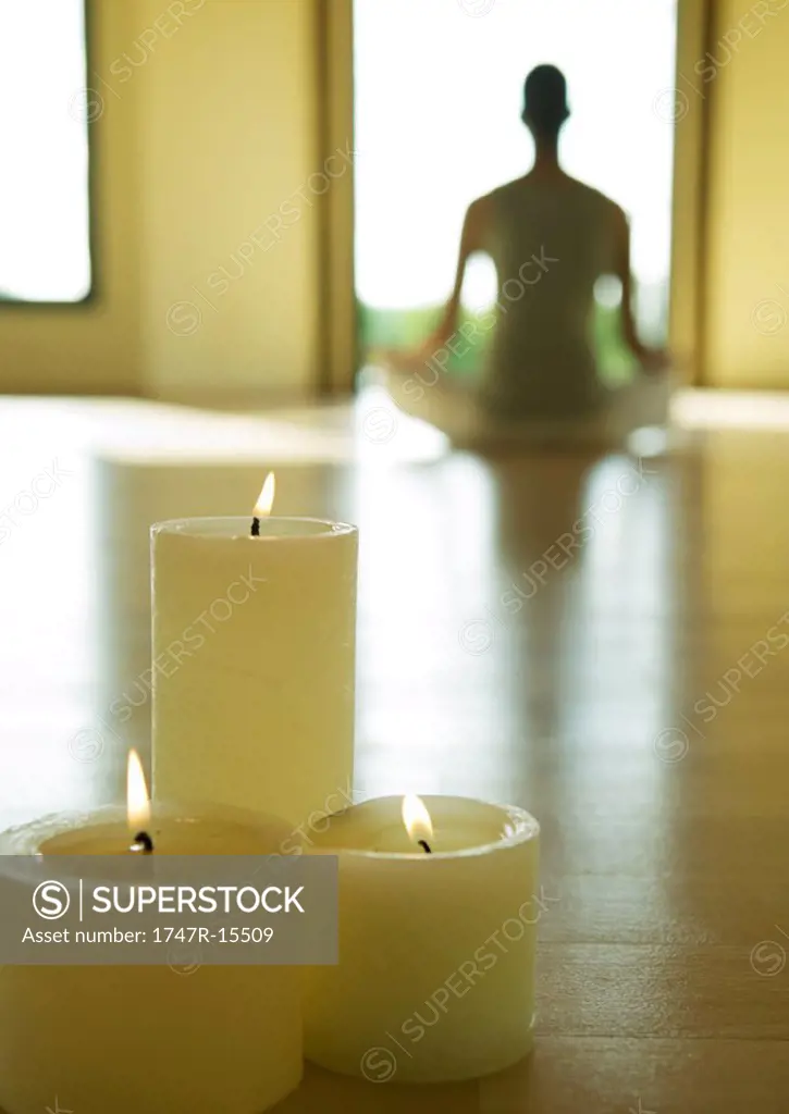 Yoga class, candles burning while person sits in lotus position in blurred background