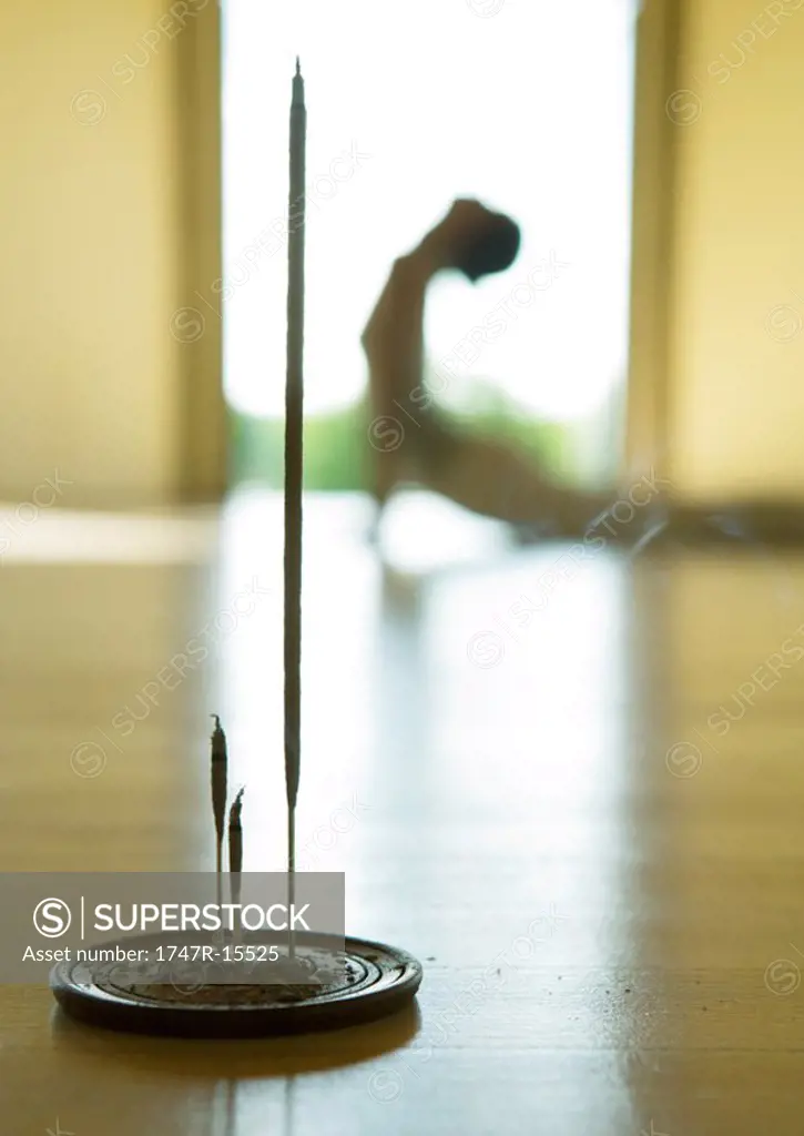 Yoga class, woman doing cobra pose, focus on incense in foreground