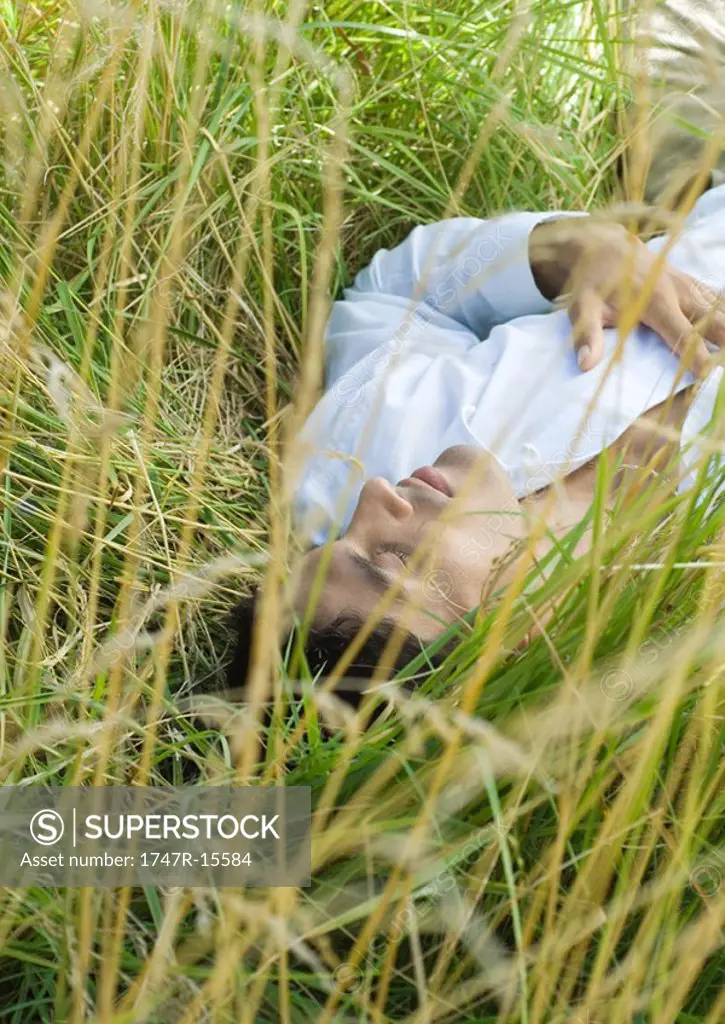Man lying in tall grass, eyes closed